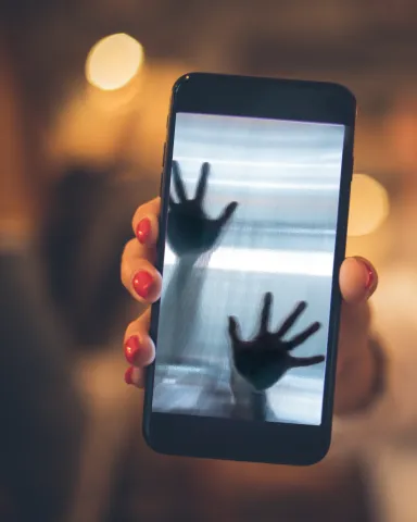 A hand holding a cellphone.  On the cellphone are 2 hands trying to get out of the phone.  