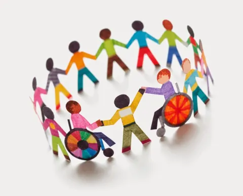 Paper cutout figures of diverse children, including some in wheelchairs, holding hands in a circle to represent inclusion and community.
